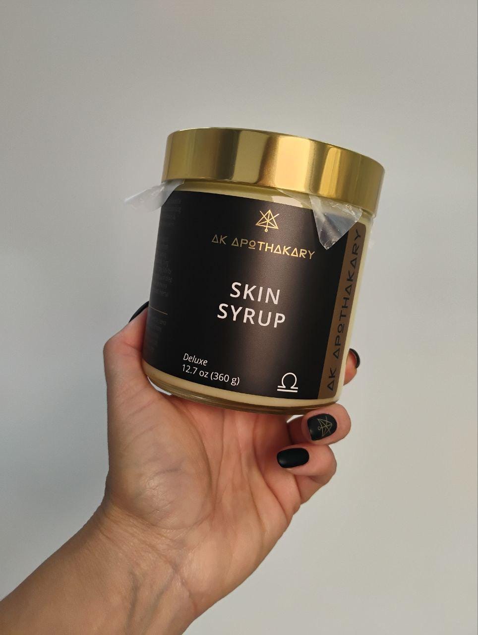 A hand holds a Deluxe jar of Skin Syrup.