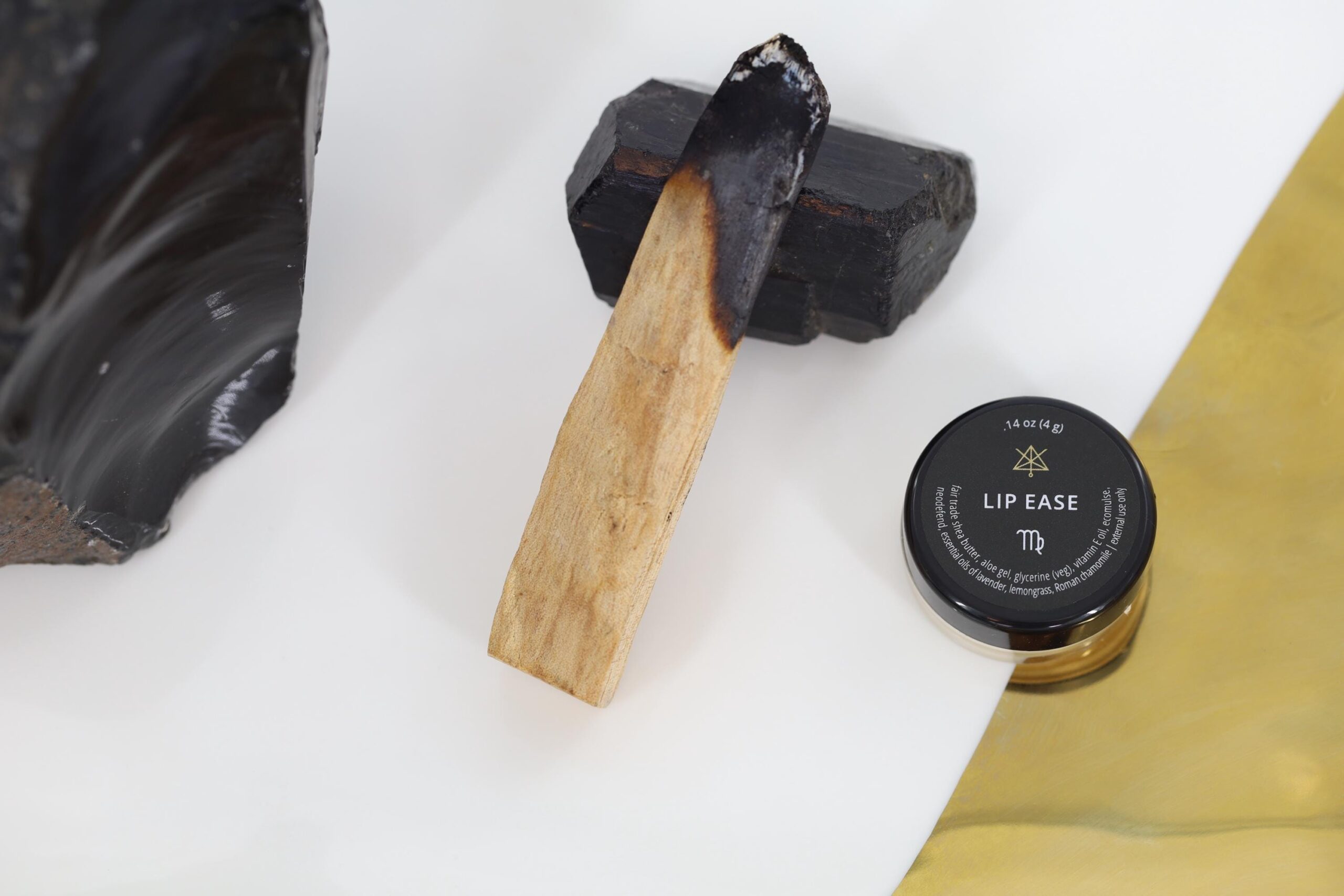 A jar of Lip ease sits next to a charred piece of wood leaned on a piece of dark crystal