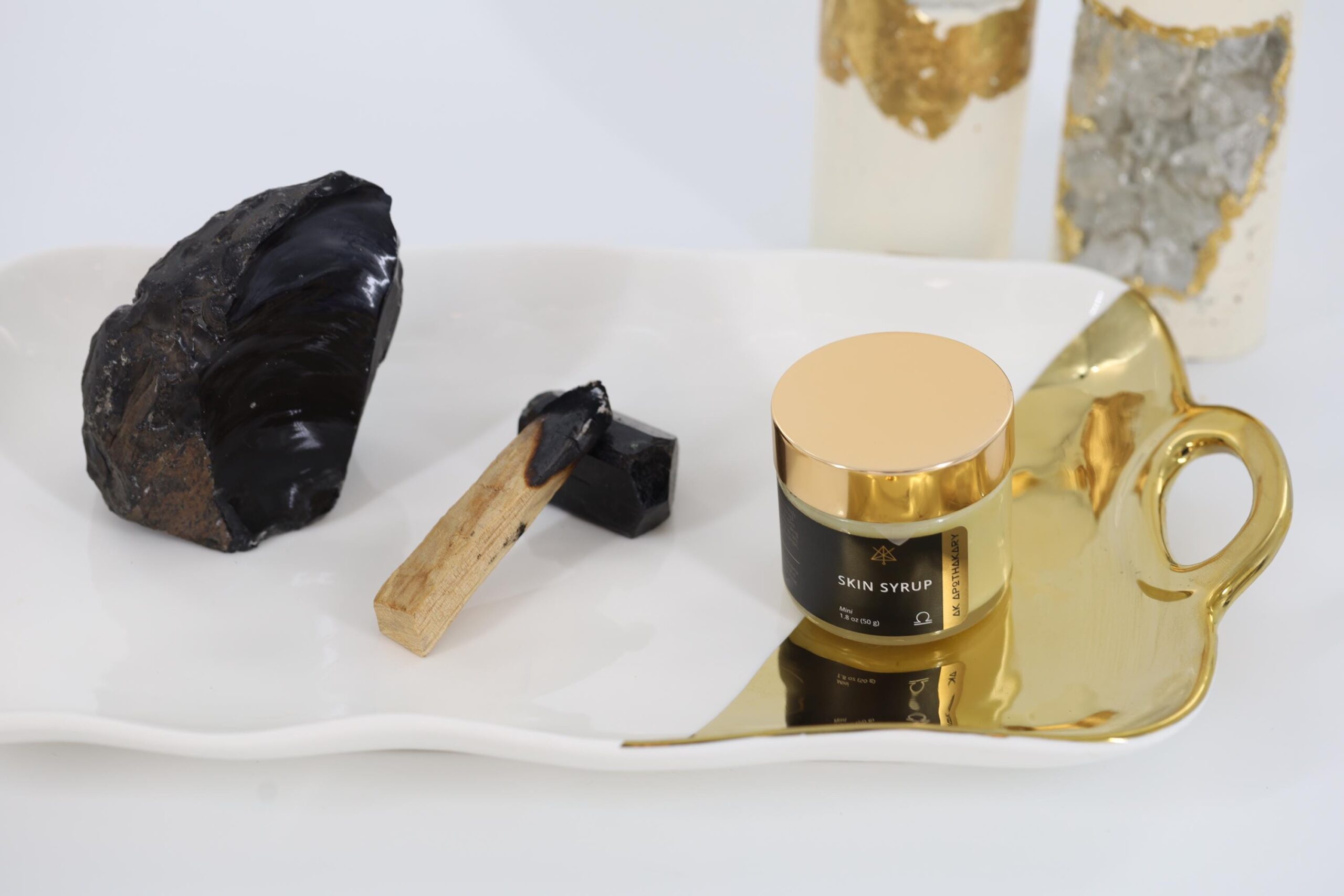 A jar of Skin Syrup sits on a tray with a large black crystal.