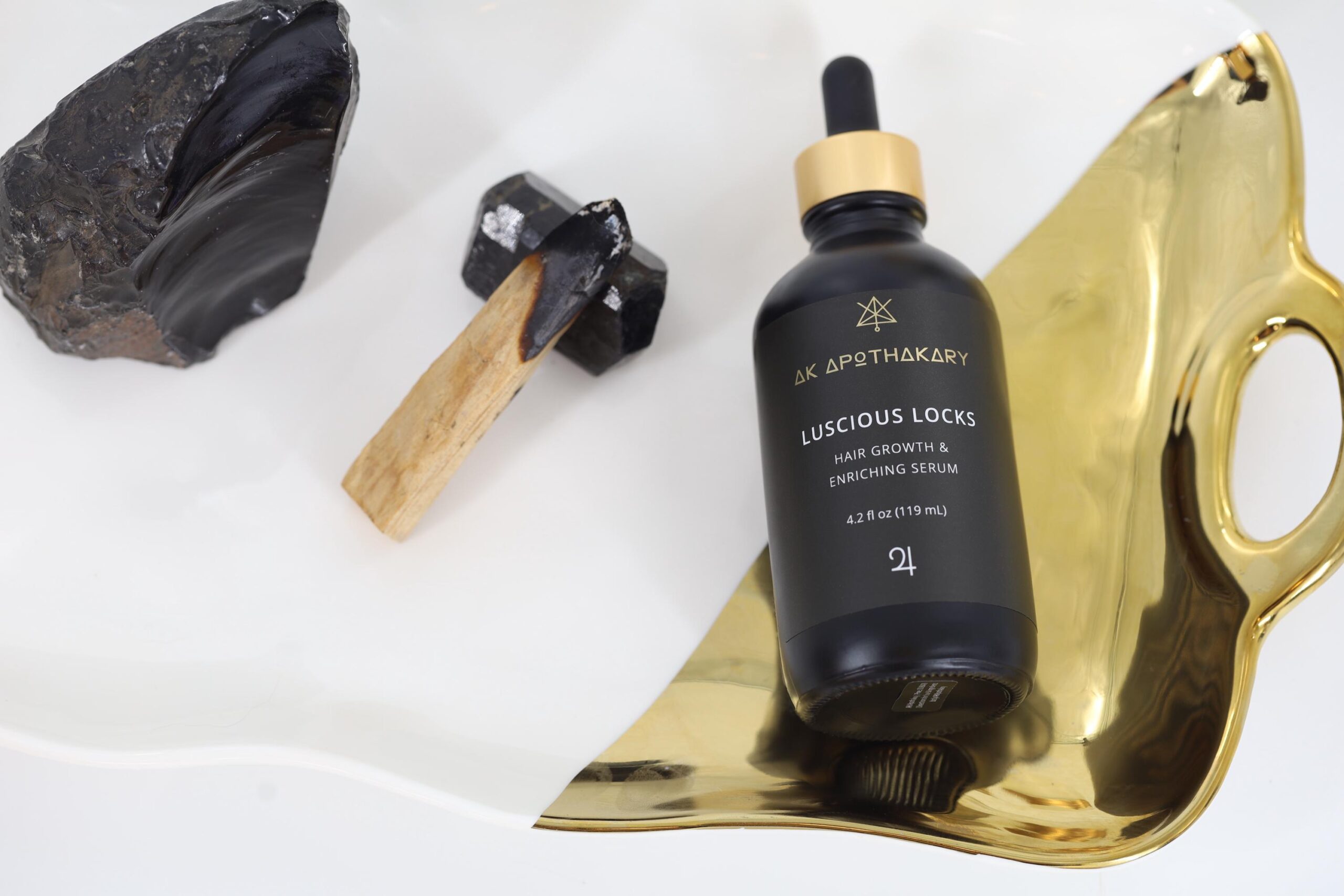 An 4.2oz eyedropper bottle of Lucios Locks sits on a gold tray next to black crystals.