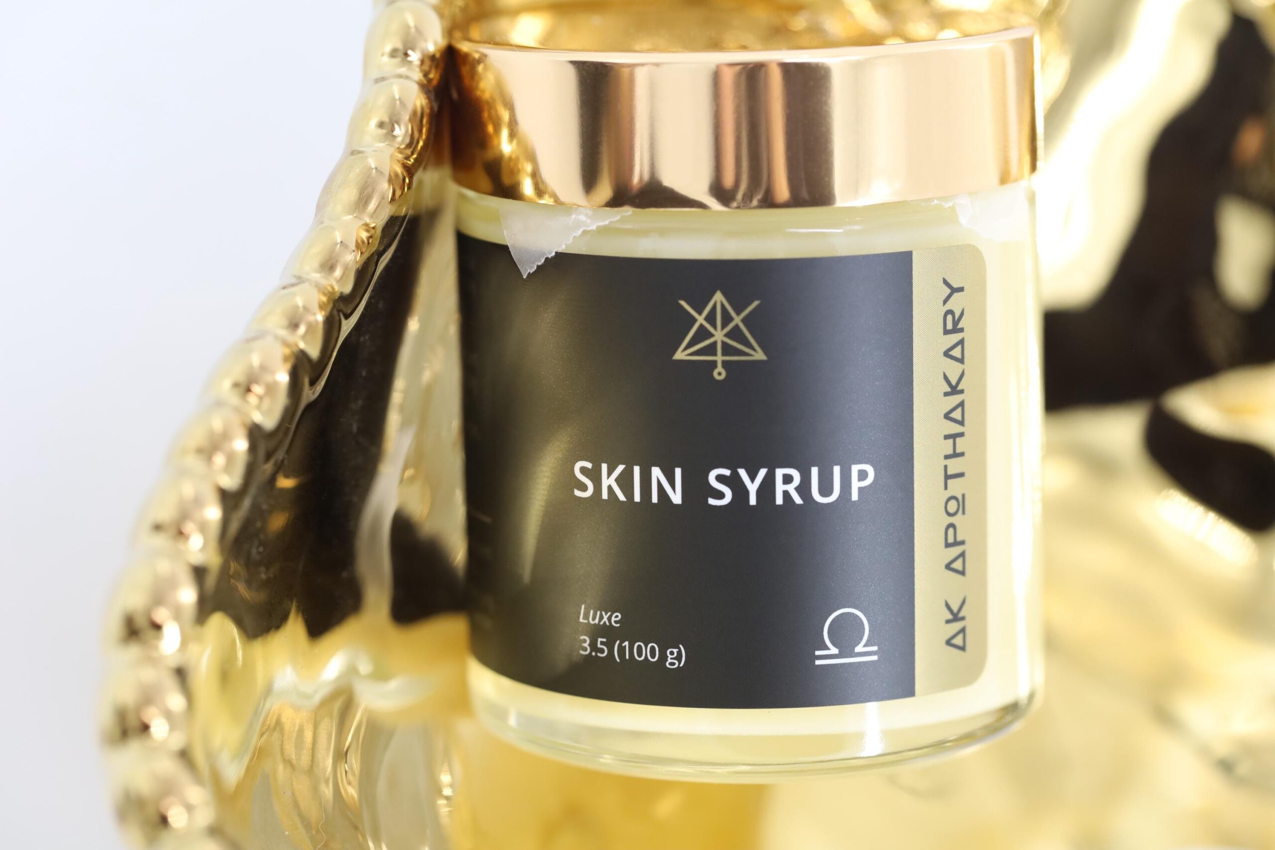 A gold topped jar of Skin Syrup sits on a gold tray.