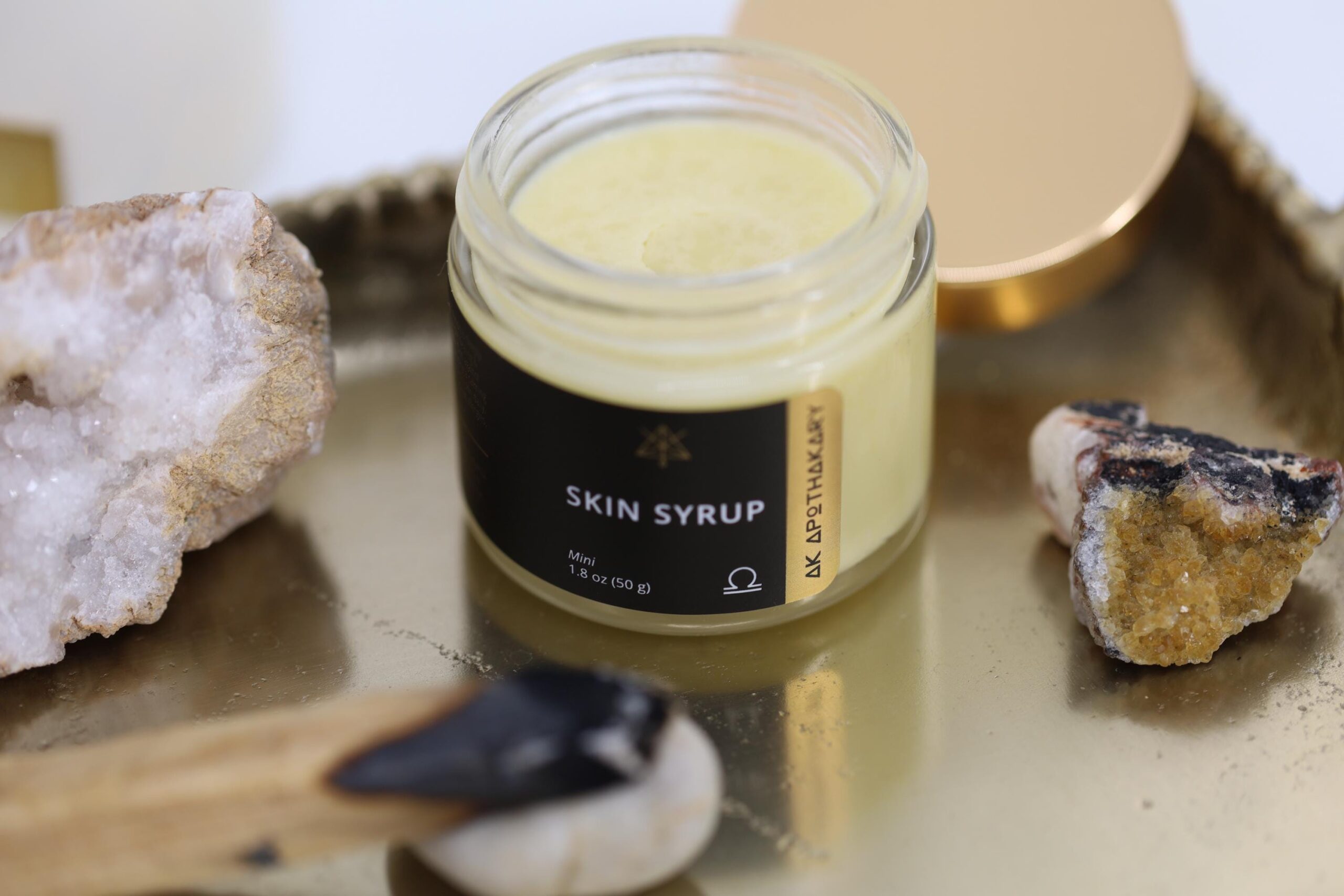 An open jr of Skin Syrup sits on a gold tray with crystals around it.
