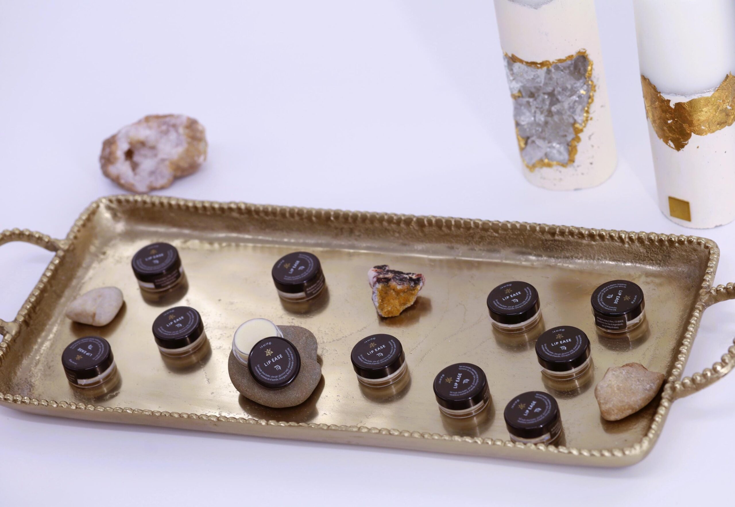 A gold tray holds multiple jars of Lip Ease and a few stones and crystals.
