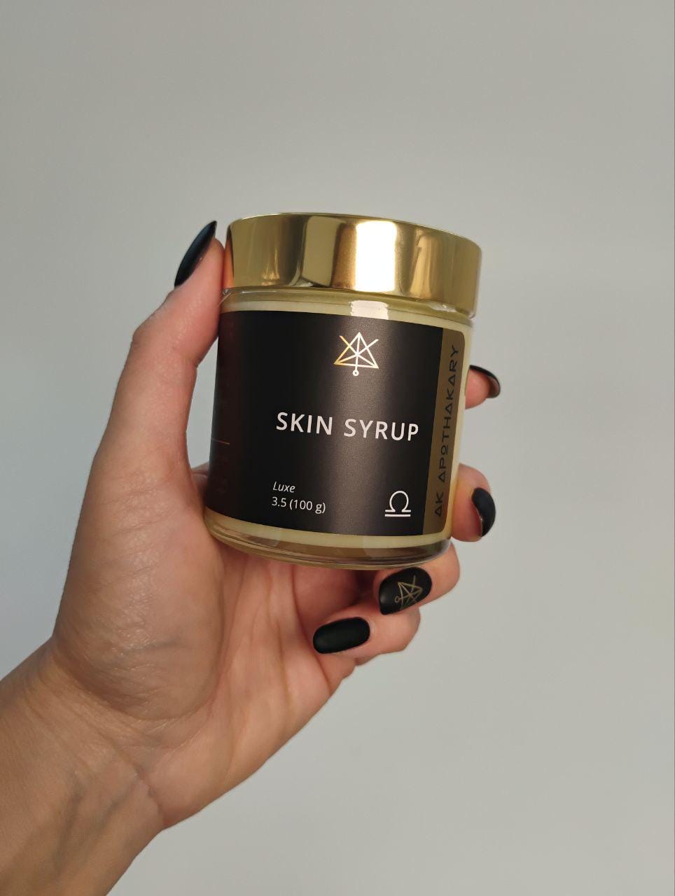 A hand holds a jar of Skin Syrup.